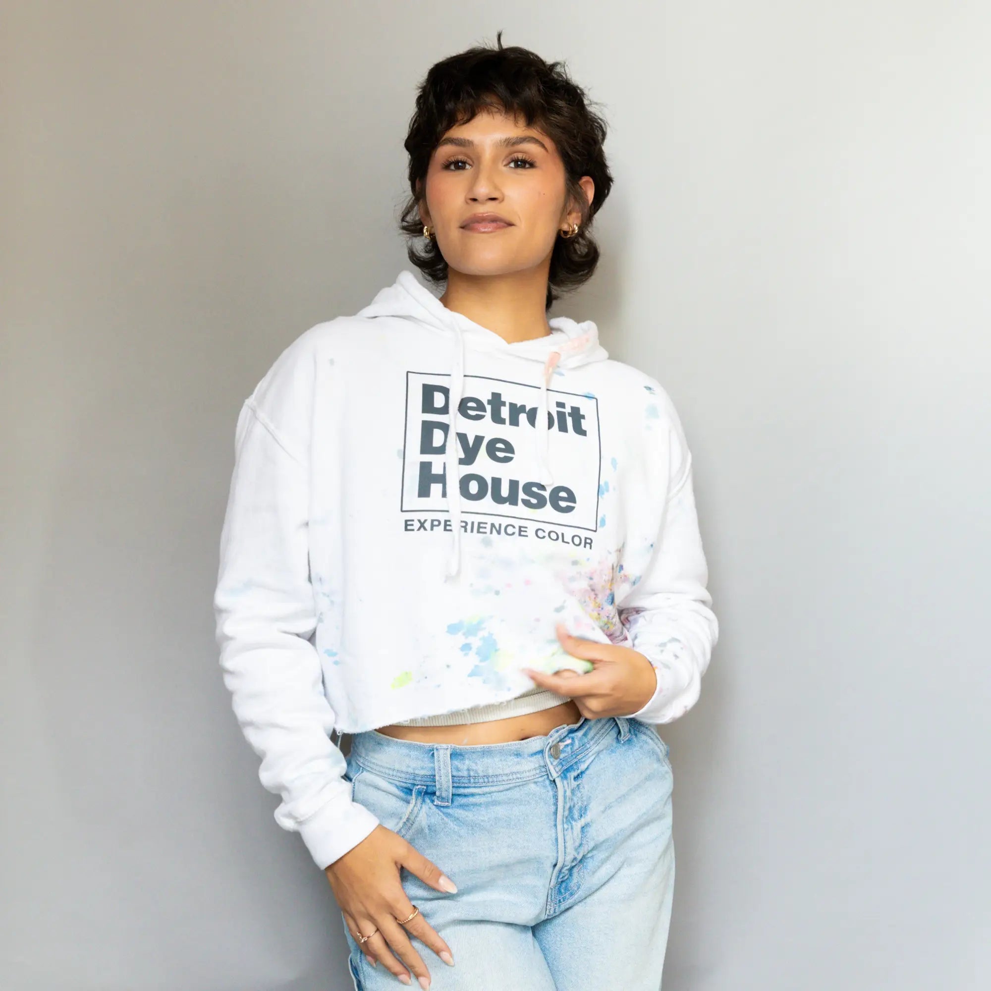 White cropped hoodie DDH with Detroit Dye House graphic paired with light blue jeans.