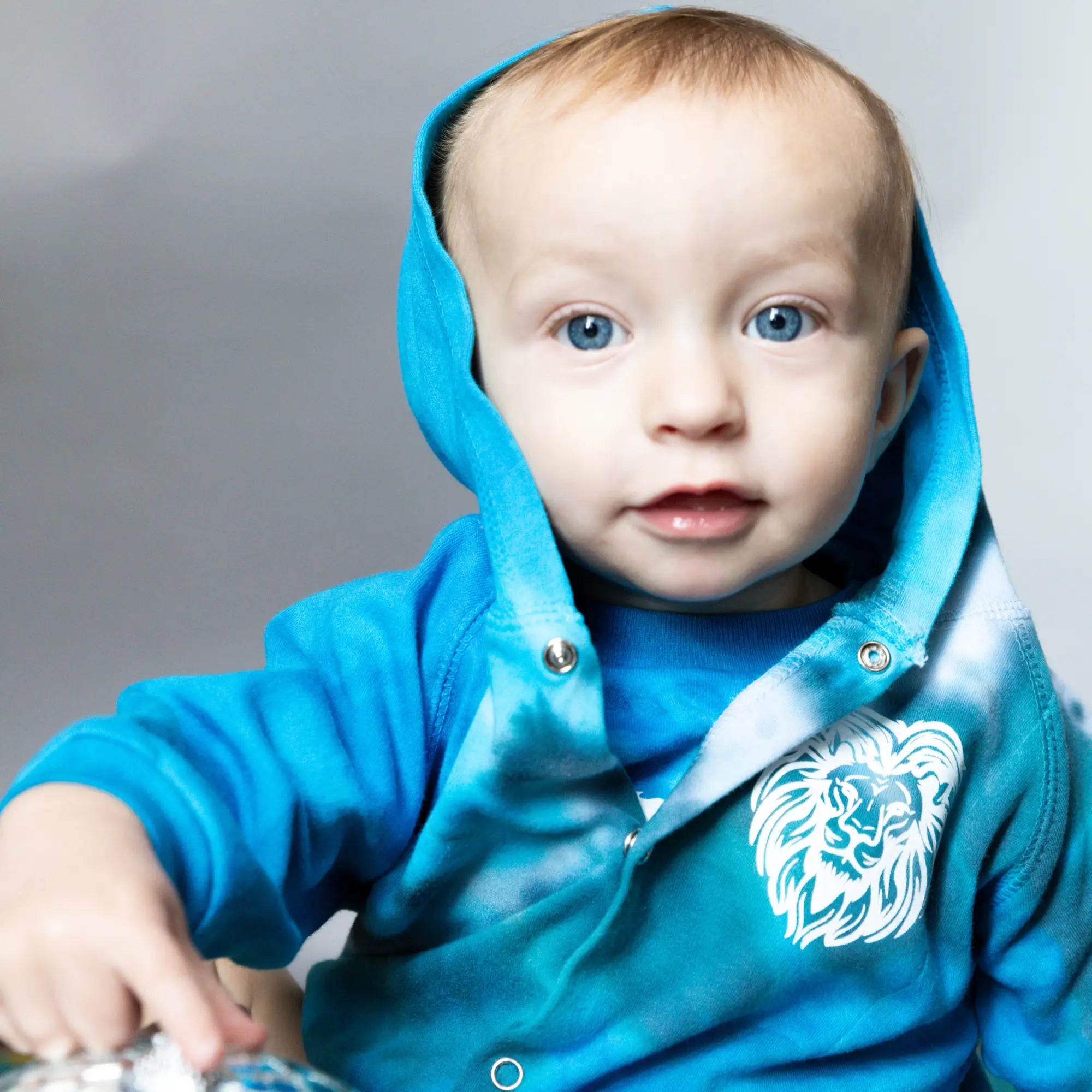 Baby in bright turquoise hooded sweatshirt with lion logo from Brightly Twisted collection.