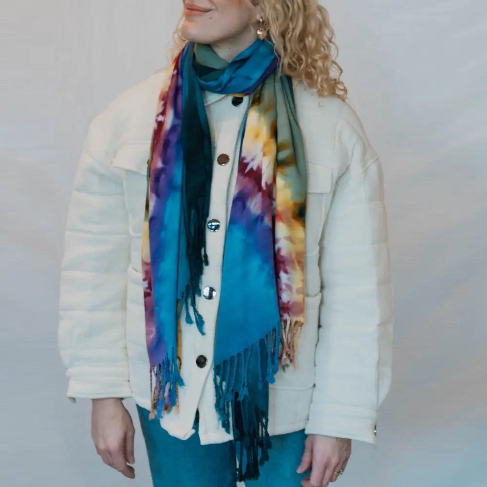 Colorful tie dye scarf with blue fringe draped over a white winter coat for stylish clothing