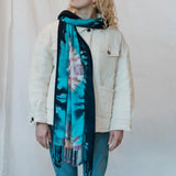 Turquoise and black tie dye scarf with fringe styled over a cream-colored jacket