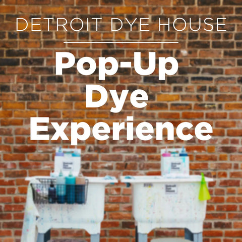 White text advertisement for Detroit Dye House Pop-Up Dye Experience on a brick wall.