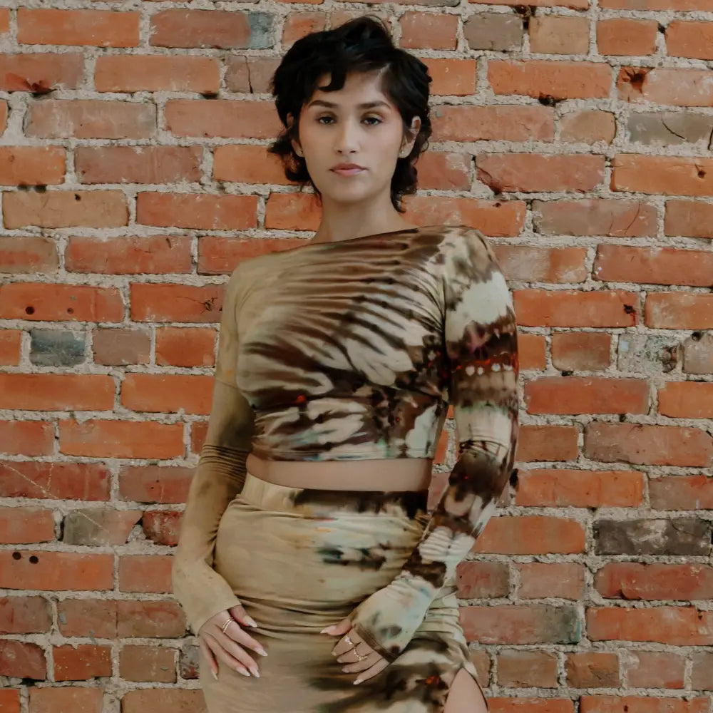 Person in a brown tie-dye crop top and maxi skirt with high slit against brick wall