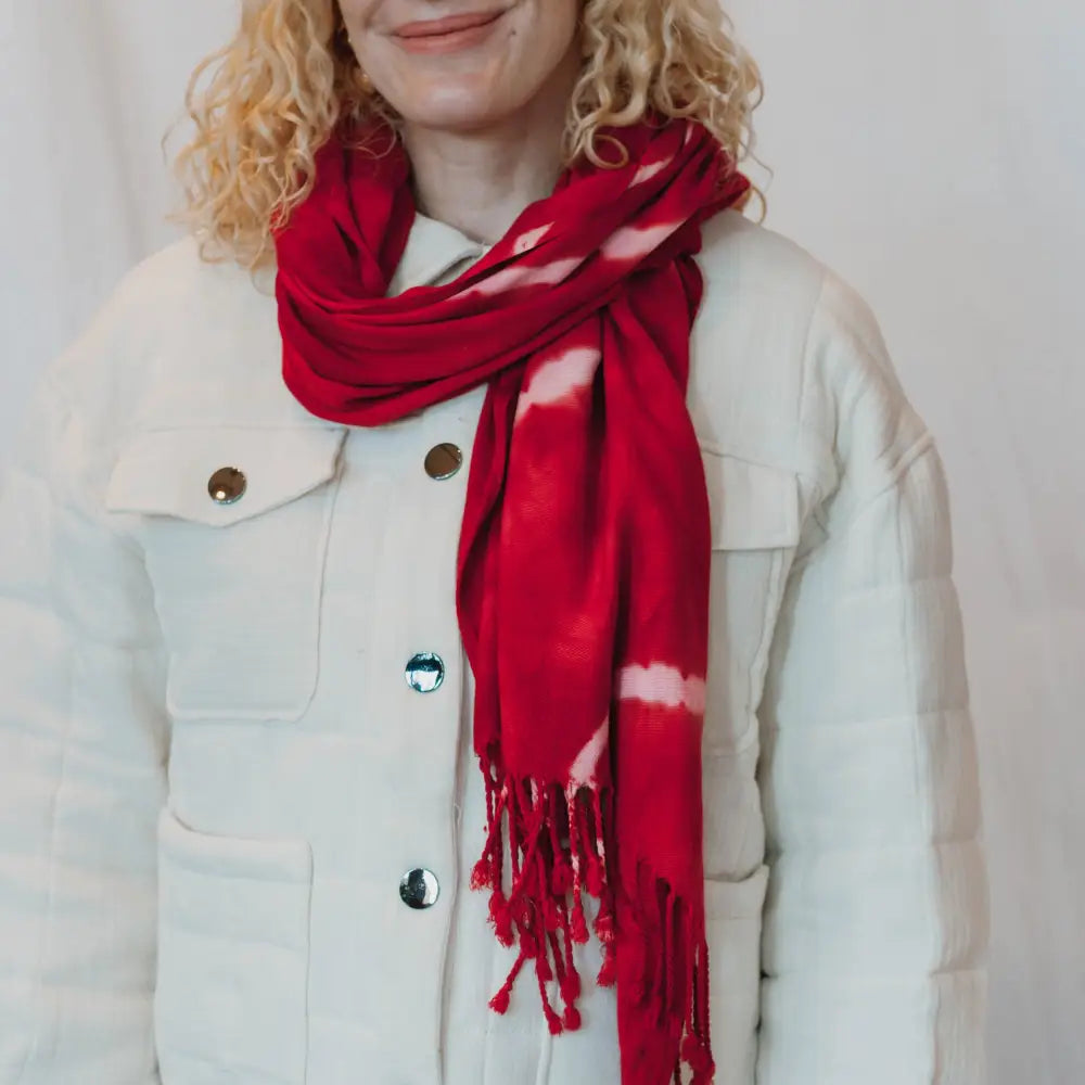 Red tie-dyed scarf with fringe wrapped around a stylish white jacket, trendy clothing accessory