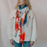 Colorful tie dye scarf in orange, blue, and white draped over a white jacket