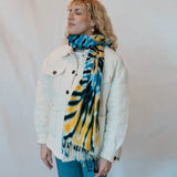 Tie-dyed blue, yellow, and black scarf accentuating a white denim jacket